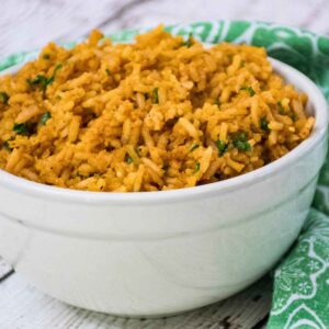 A white bowl filled with fluffy Spanish rice garnished with bits of fresh parsley, set on a green patterned cloth.