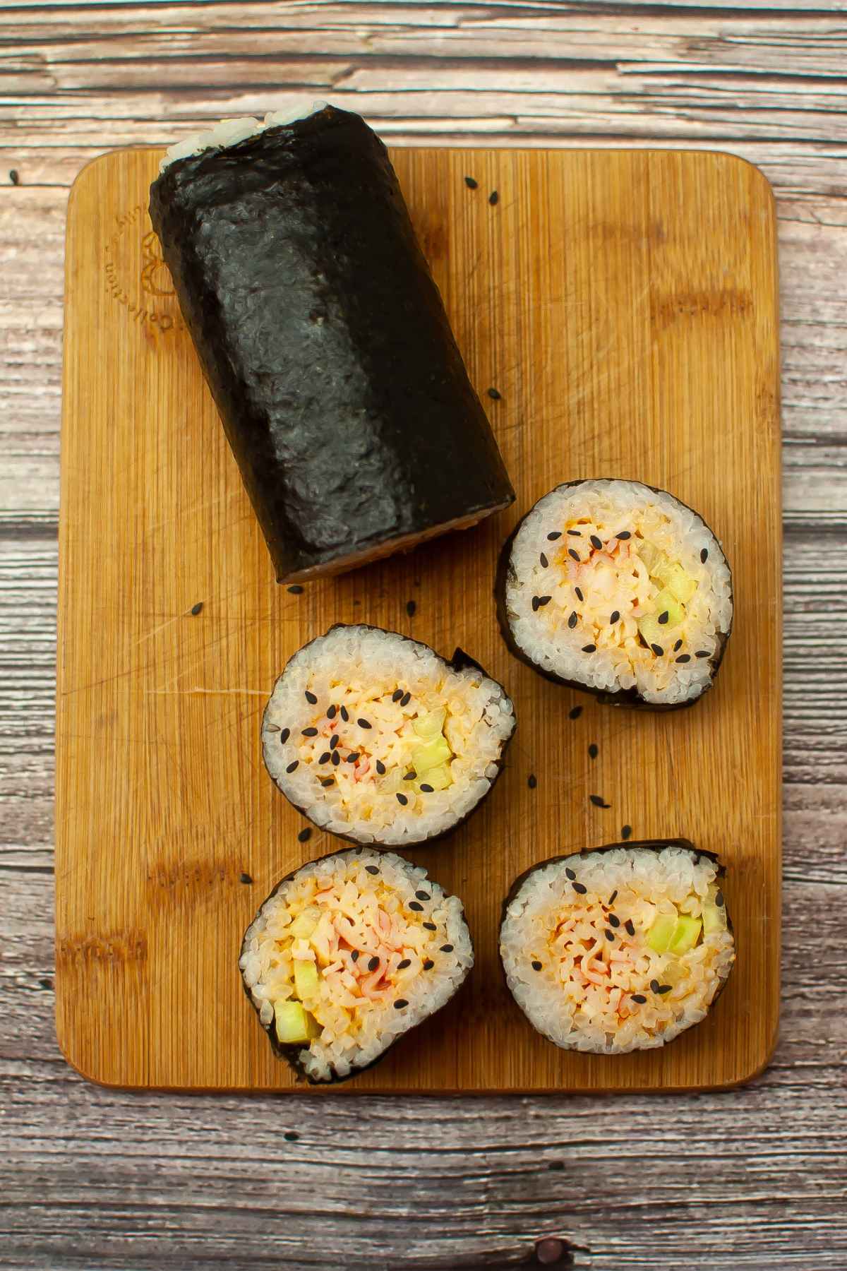 A sushi roll wrapped ini seaweed and cut into pieces showing spicy crab and cucumber filling, displayed on a wooden cutting board.