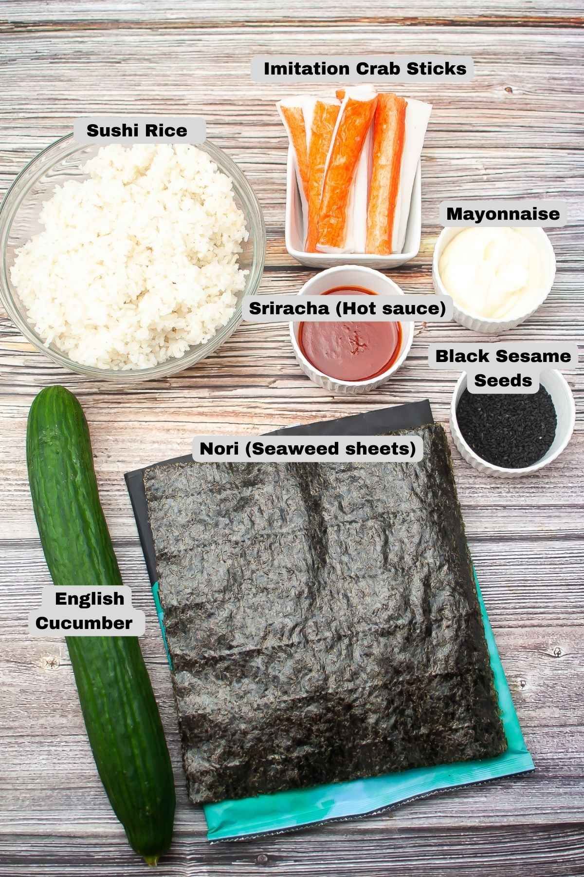 Ingredients for making sushi rolls displayed: bowl of sushi rice, imitation crab sticks, mayonnaise, sriracha, black sesame seeds, English cucumber, and nori seaweed sheets.