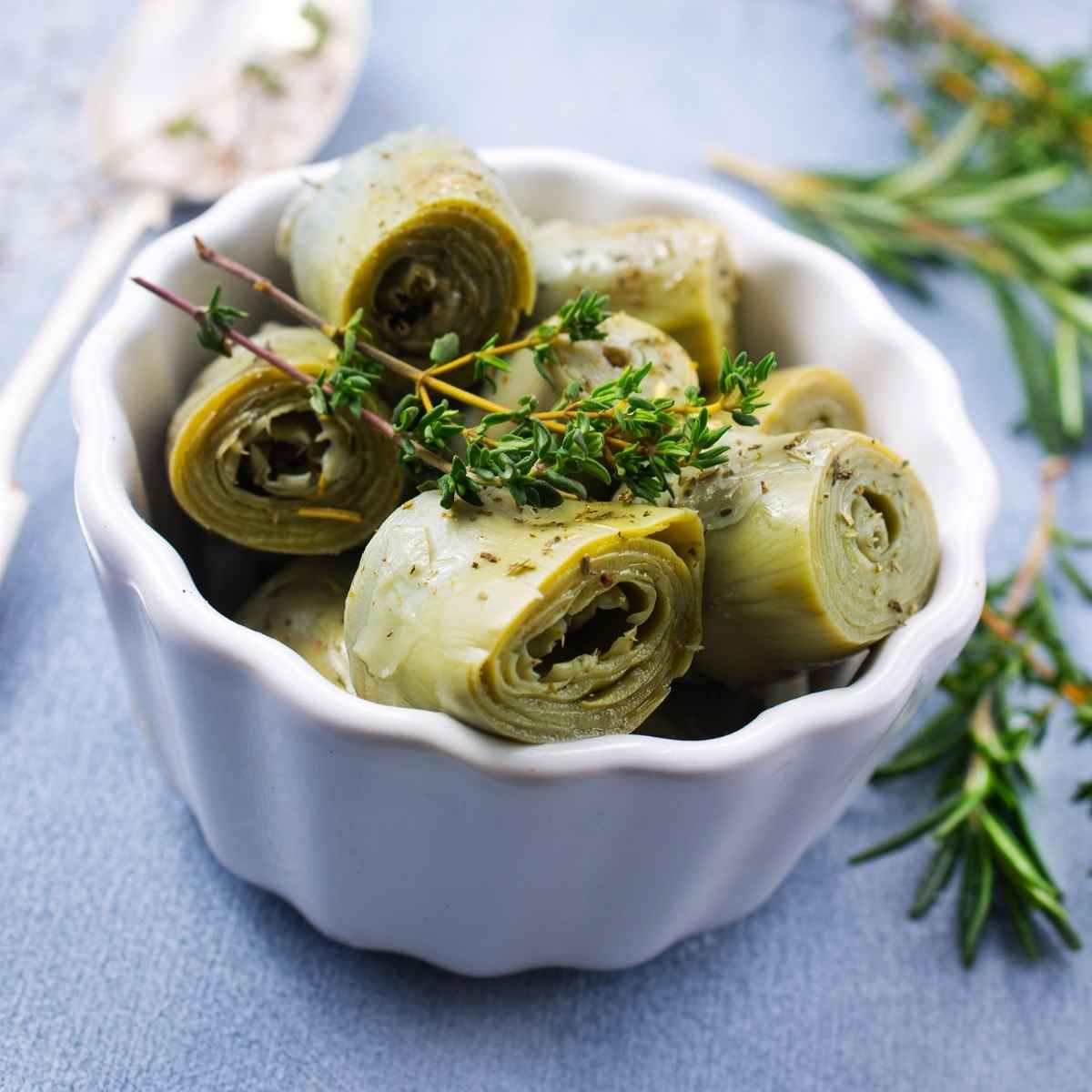 A white bowl filled with marinated artichoke hearts, garnished with sprigs of fresh herbs.