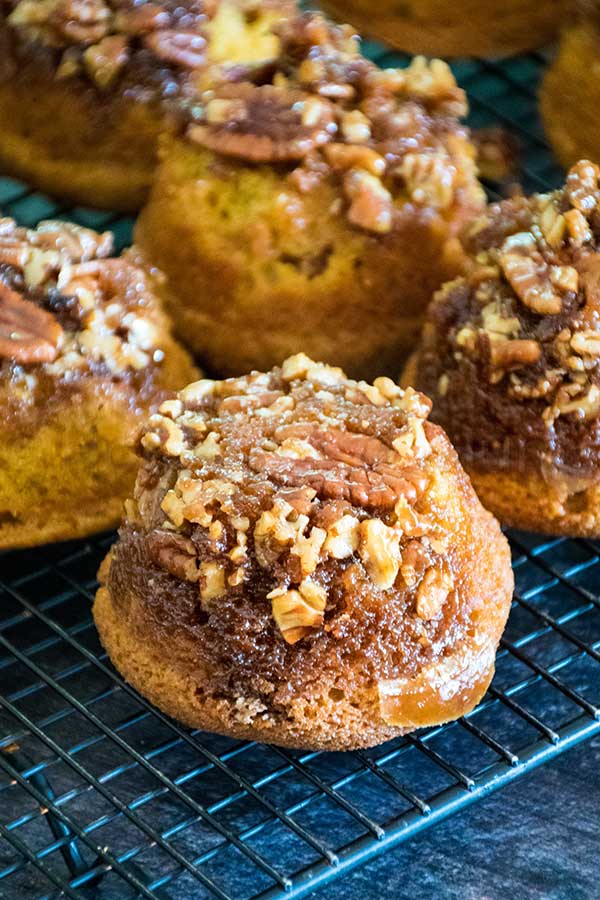 Pecan praline pumpkin muffin topped with chopped pecans and brown sugar glaze, cooling on a wire rack.