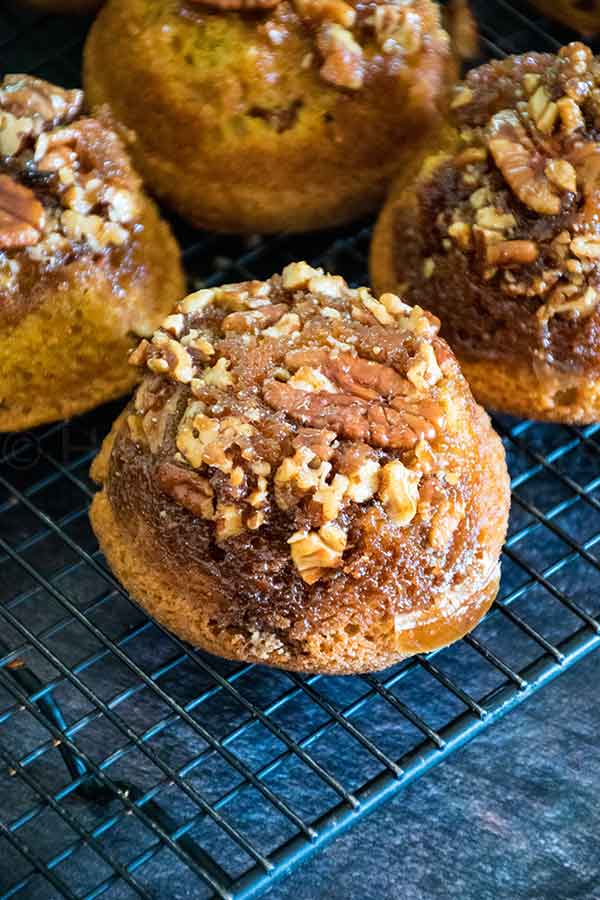 Pecan praline pumpkin muffin topped with chopped pecans and brown sugar glaze, cooling on a wire rack.