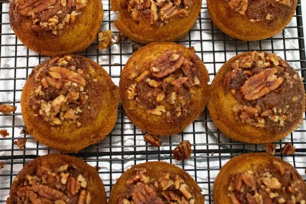 Overhead view of sticky bun pumpkin muffins cooling on a wire rack, each muffin topped with chopped pecans and caramelized glaze.