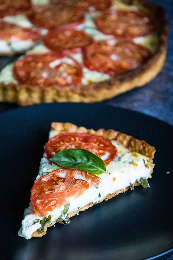 Slice of tomato pie with cheese filling and fresh basil and tomato slices on a black plate.