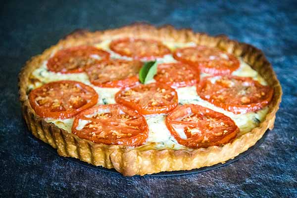 Whole Baked Tomato Basil Ricotta Tart with sliced tomatoes and garnished with basil.