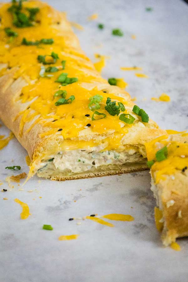 Golden baked tuna crescent braid sliced open, showing the creamy tuna filling inside, topped with cheddar cheese and green onions.
