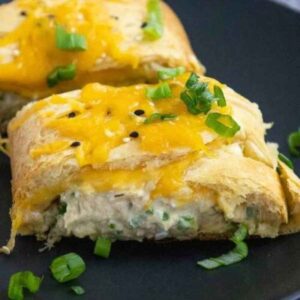 Two slices of tuna crescent braid on a black plate, topped with melted cheddar and green onions with the creamy tuna fulling visible.