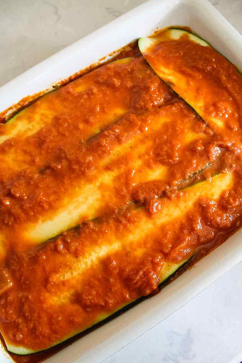 A baking dish with zucchini slices layered and topped with rich red vodka sauce.