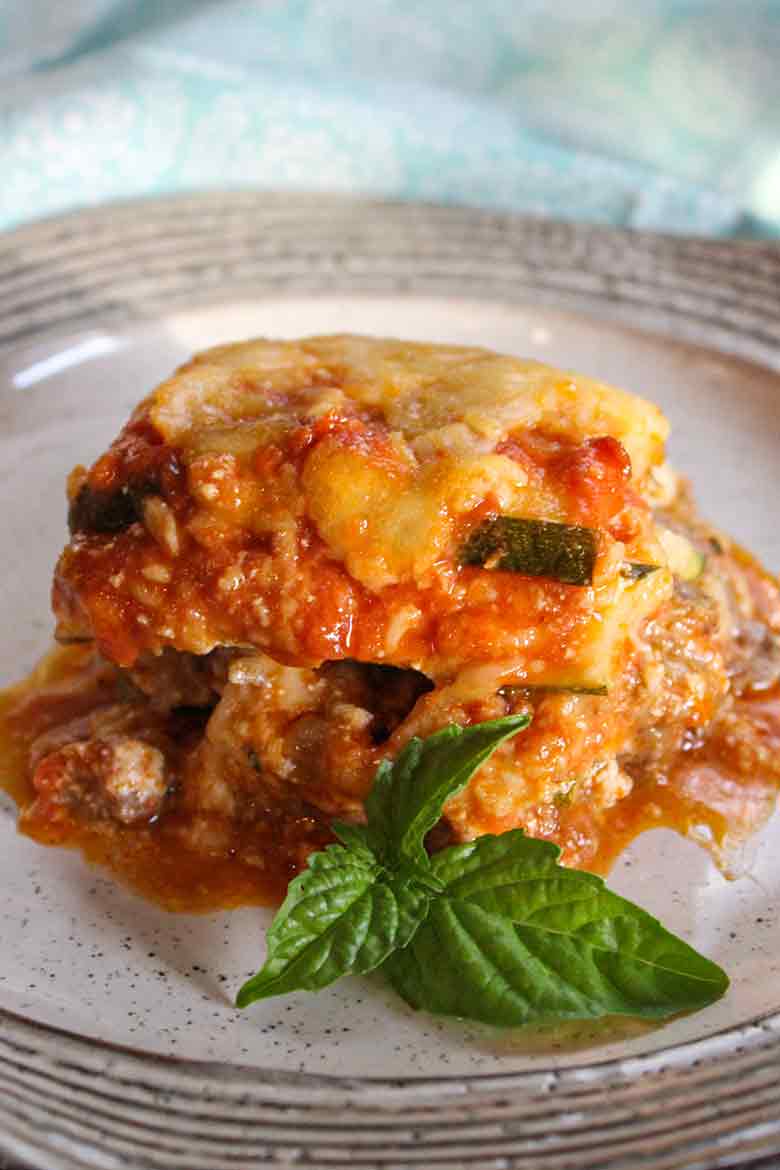 A serving of zucchini lasagna on a white plate, garnished with a fresh basil leaf.