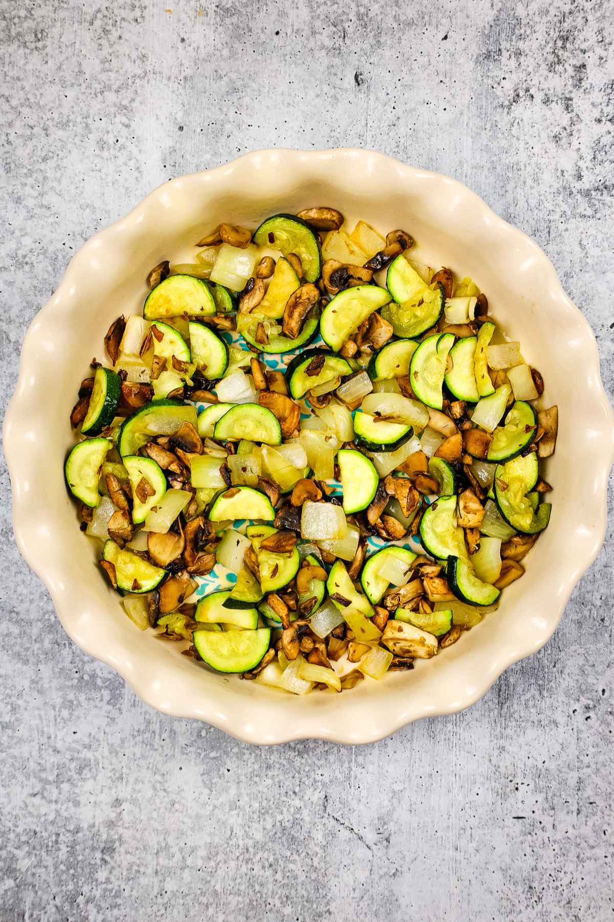 Roasted zucchini, onions, and mushrooms arranged in a pie dish.