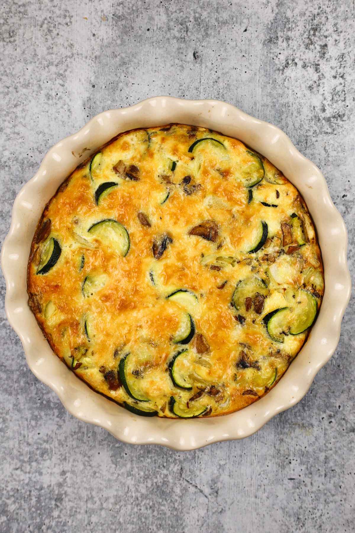Whole zucchini mushroom quiche baked in a scalloped ceramic dish with a browned top.