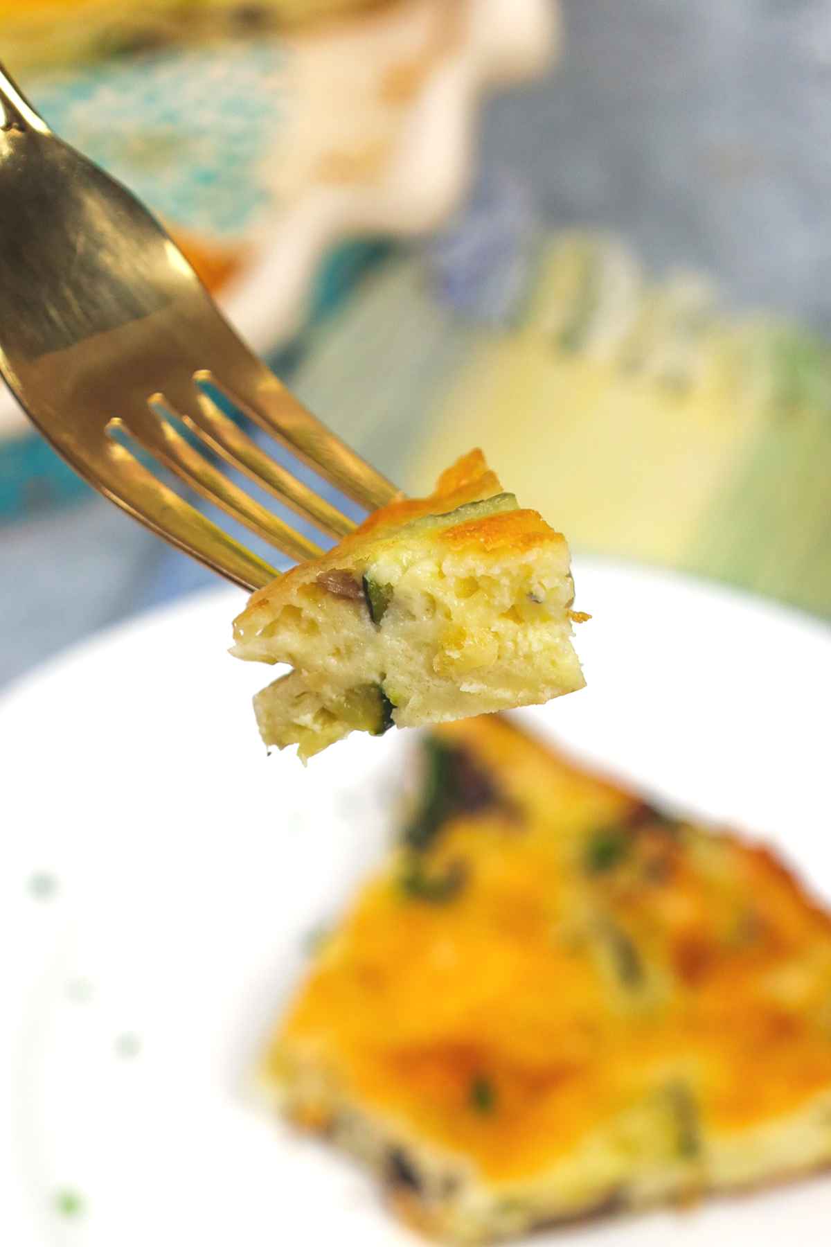Close up bite of quiche on a gold fork showing tender crustless filling.