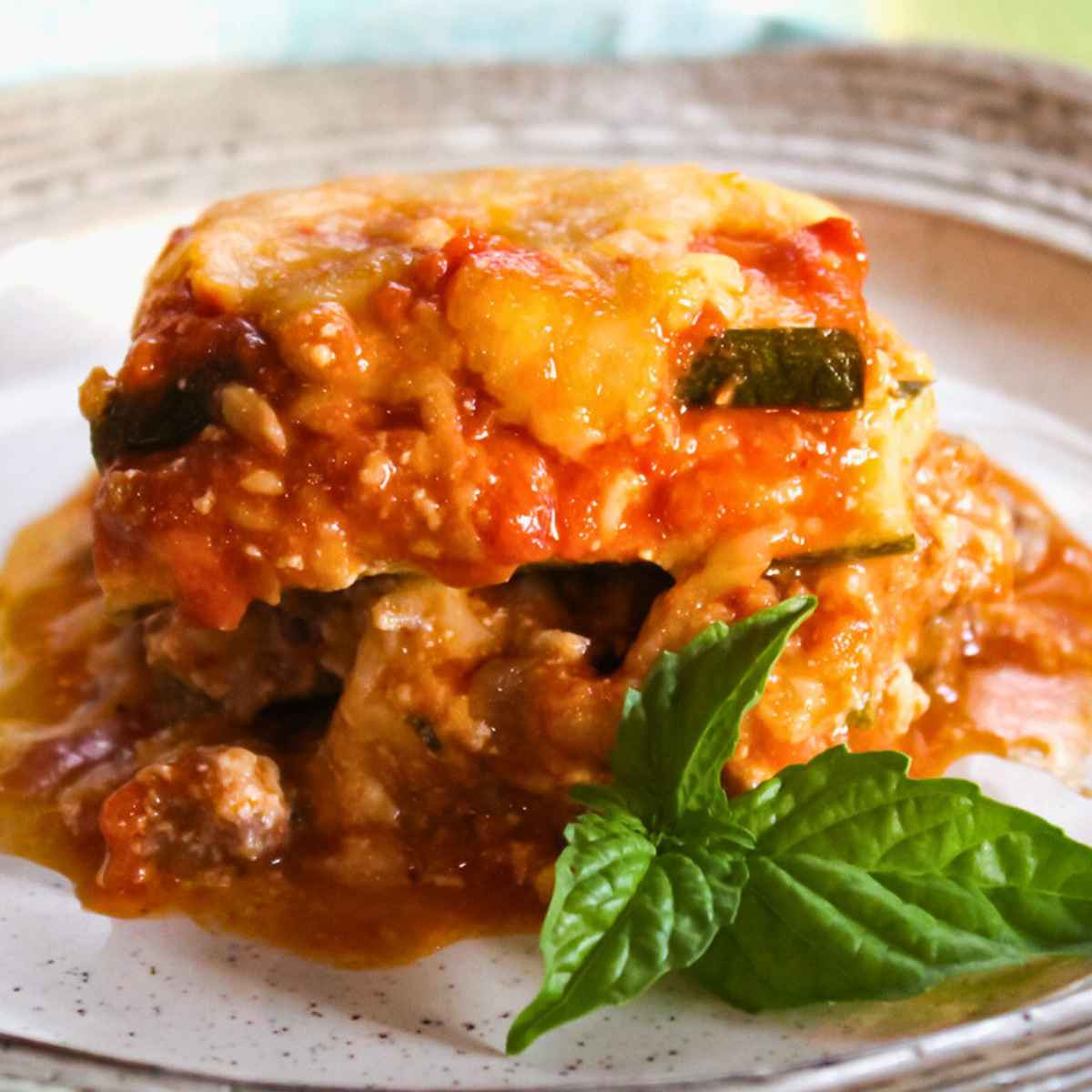 A serving of zucchini lasagna on a white plate, garnished with a fresh basil leaf.