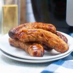 Close up of juicy air fryer sausage links stacked on a white plate, highlighting their browned, crispy exterior.