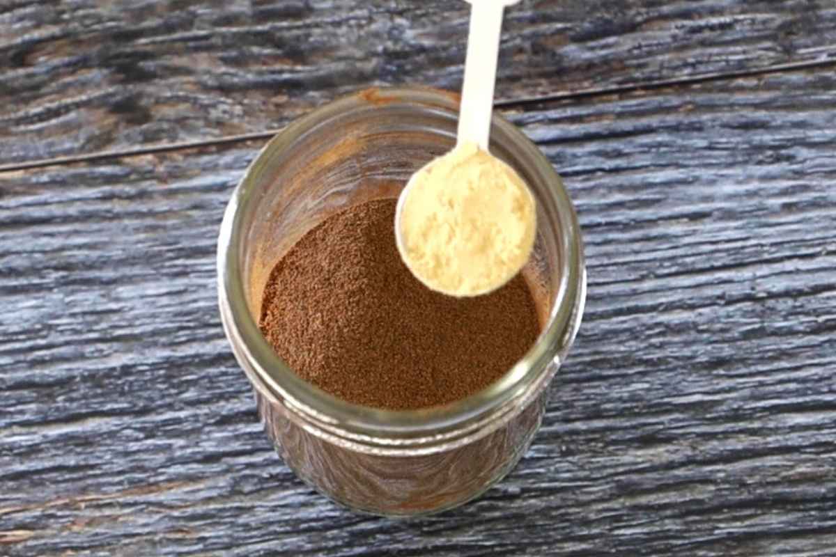 A jar of apple pie spice with a measuring spoon of ground ginger being added on top.