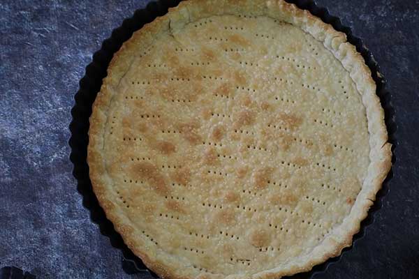 Baked tart shell with golden crust and fork marks in the base.