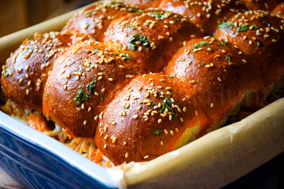Freshly baked sliders in a baking dish with golden sesame topped buns