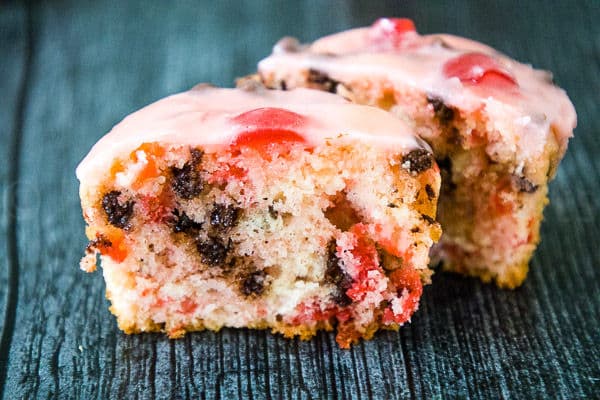 A cherry chocolate chip muffin cut in half, showing the inside texture with chocolate chips and cherry pieces, topped with pink glaze.