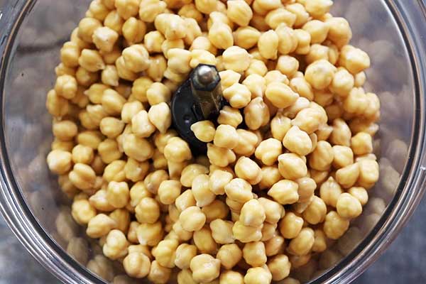 A food processor bowl filled with soaked chickpeas, ready to be blended.