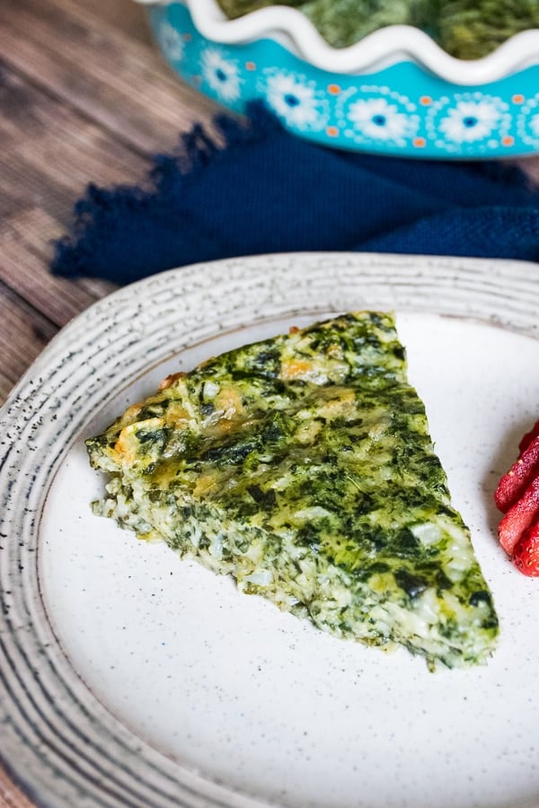 A slice of crustless spinach quiche on a plate with sliced strawberries on the side.