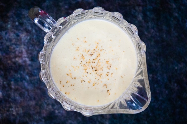 Overhead view of a glass pitcher filled with homemade eggnog, sprinkled with nutmeg.