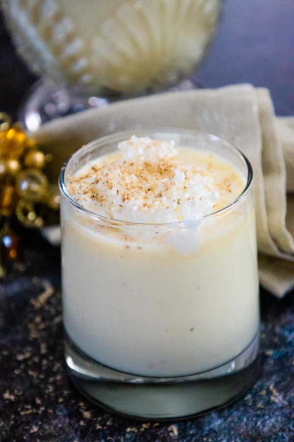 Glass of homemade eggnog topped with whipped cream and a sprinkle of nutmeg.