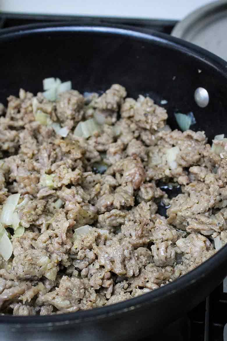 Crumbled Italian Turkey Sausage with diced onions browning in a black skillet.