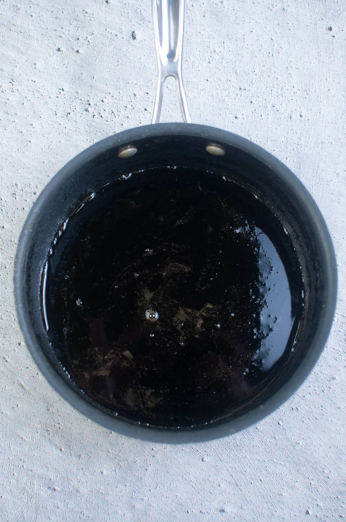 Saucepan filled with dark syrup mixture on a light gray surface.