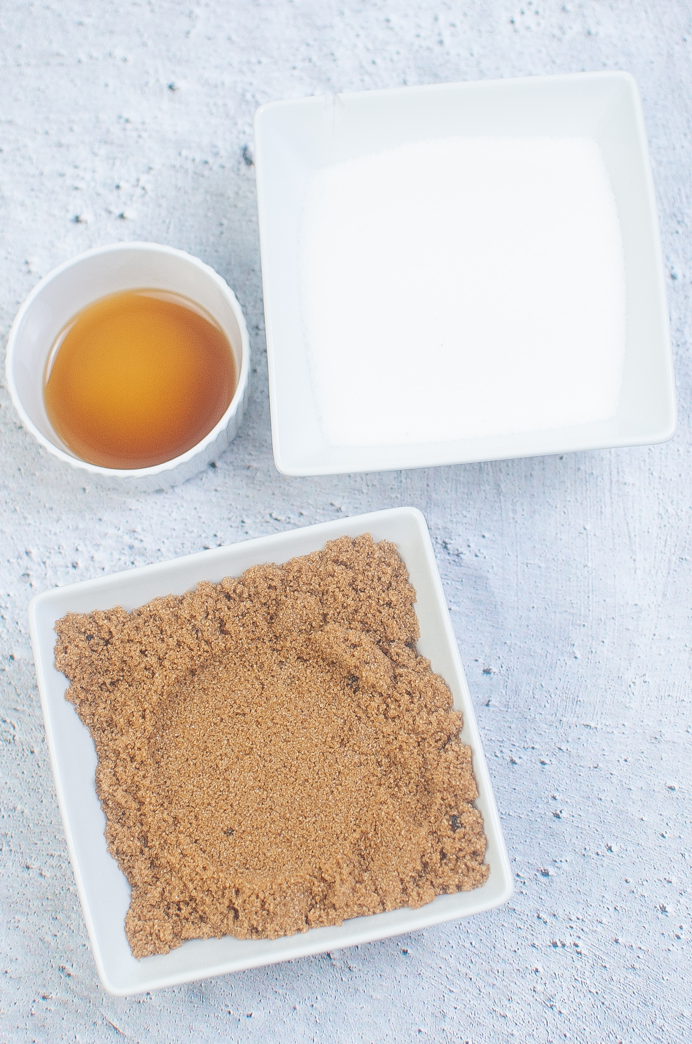 Overhead view of ingredients: a bowl of brown sugar, a bowl of white sugar, and a small bowl of maple extract.