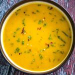 Overhead view of a bowl of creamy pumpkin soup garnished with chopped chives and red pepper flakes.