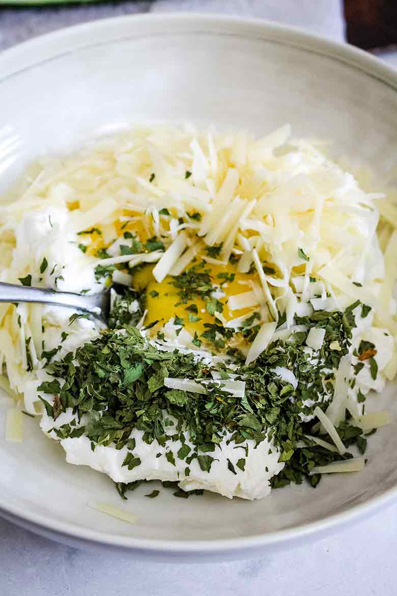 A mixing bowl filled with ricotta cheese, shredded parmesan, egg, and chopped parsley.