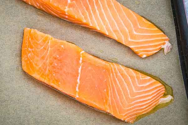 Raw salmon fillets on a sheet pan lined with parchment paper.