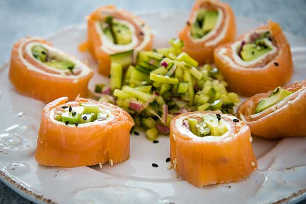 Sliced salmon sushi rolls filled with avocado and cucumber arranged on a plate with a small pile of cucumber salad.
