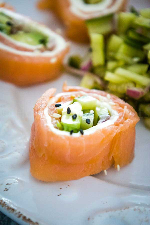 Close up of Salmon Sushi Roll with avocado, cucumber, cream cheese, and black and white sesame seeds served with a cucumber salad on the side.