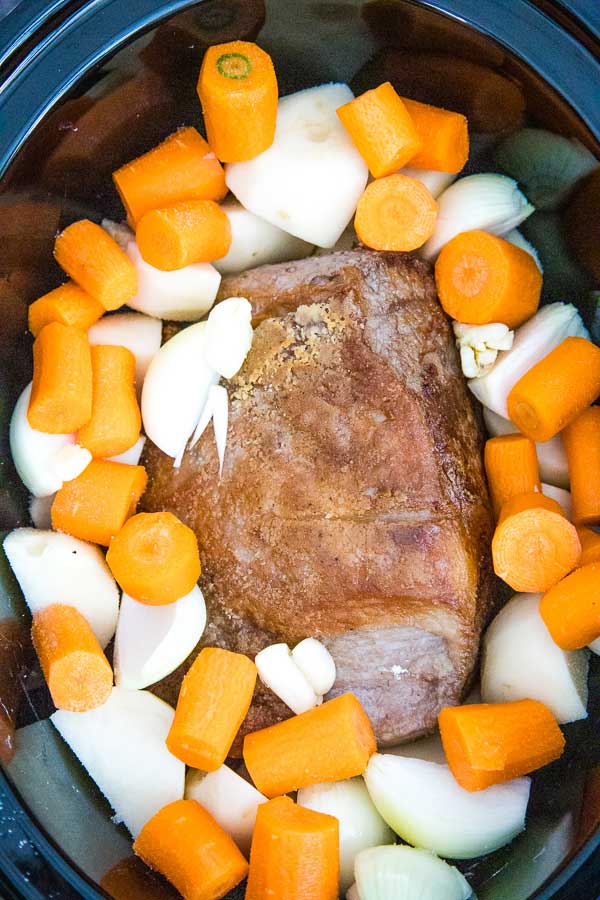 Overhead view of a seasoned beef chuck roast surrounded by chunks of carrots, onions, and garlic cloves before cooking.