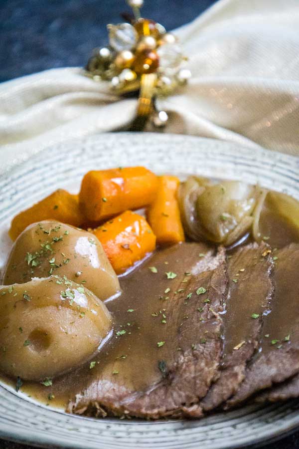 Slices of slow cooked beef chuck roast on a plate with potatoes, carrots, and onions smothered in rich gravy.