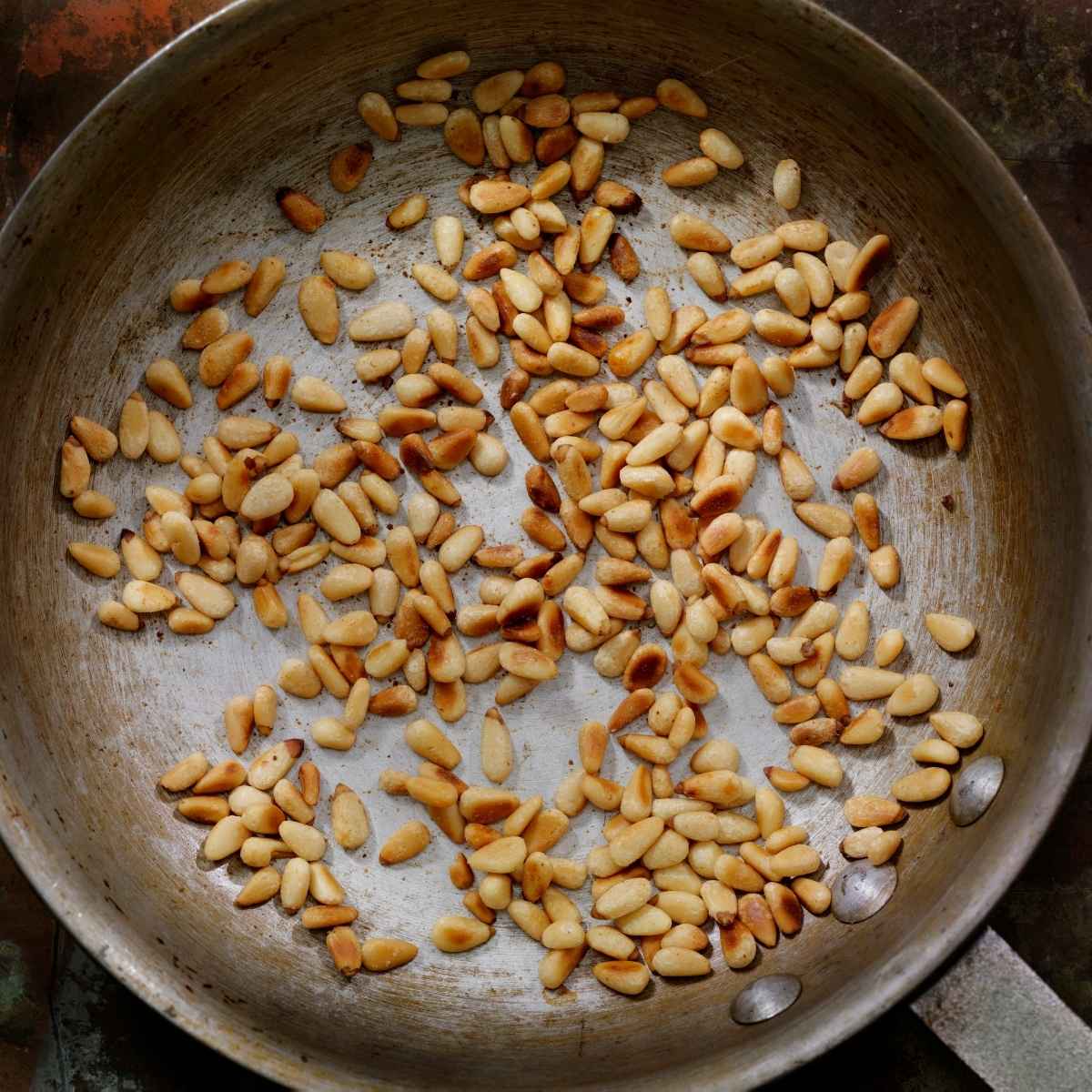 Golden brown toasted pine nuts scattered across a skillet.