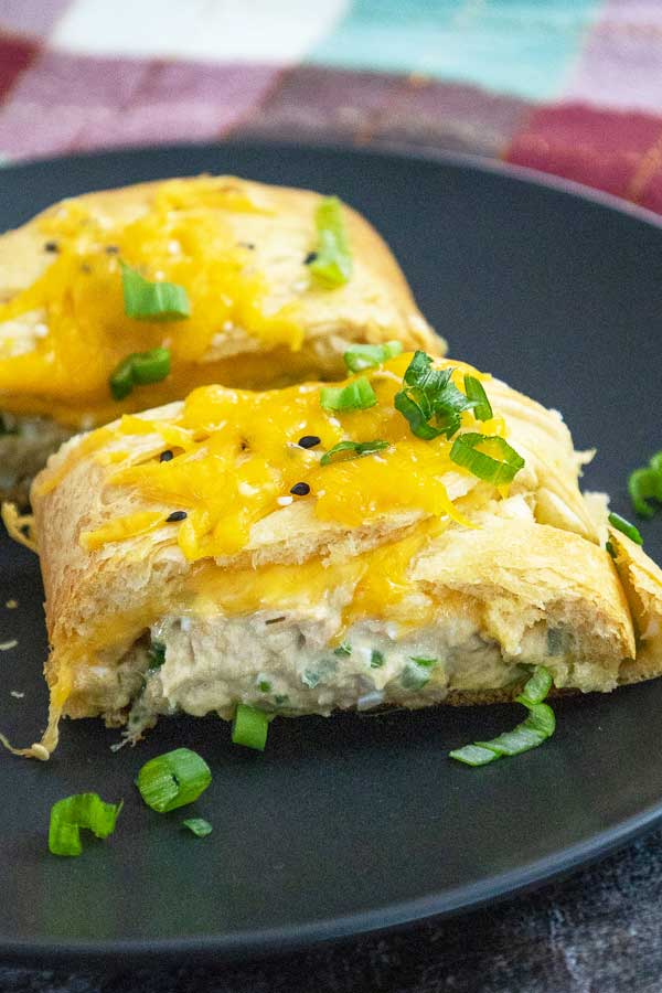 Sliced tuna crescent braid on a black plate with melted cheese topping and green onion garnish.