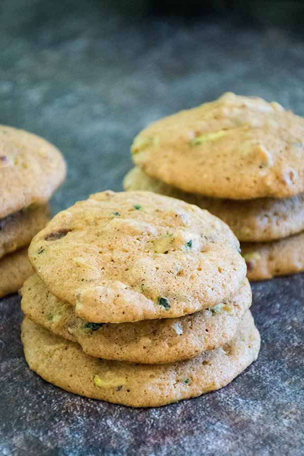 Stack of soft zucchini spice cookies on a dark countertop, showing bits of zucchini and mix-ins.