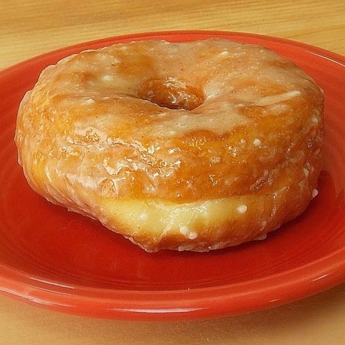 Golden apple cider glazed donut served on a red plate, showcasing the sweet cider glaze and fluffy yeast texture.