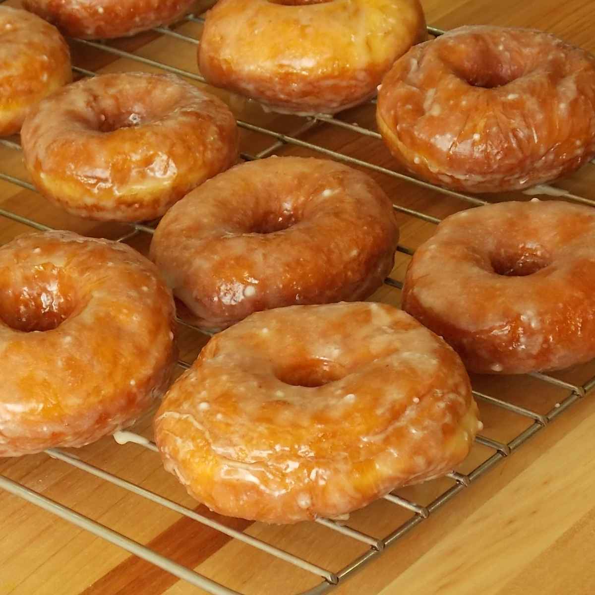 Homemade apple cider donuts dipped in apple cider glaze cooling on a wire rack, perfect for fall baking.