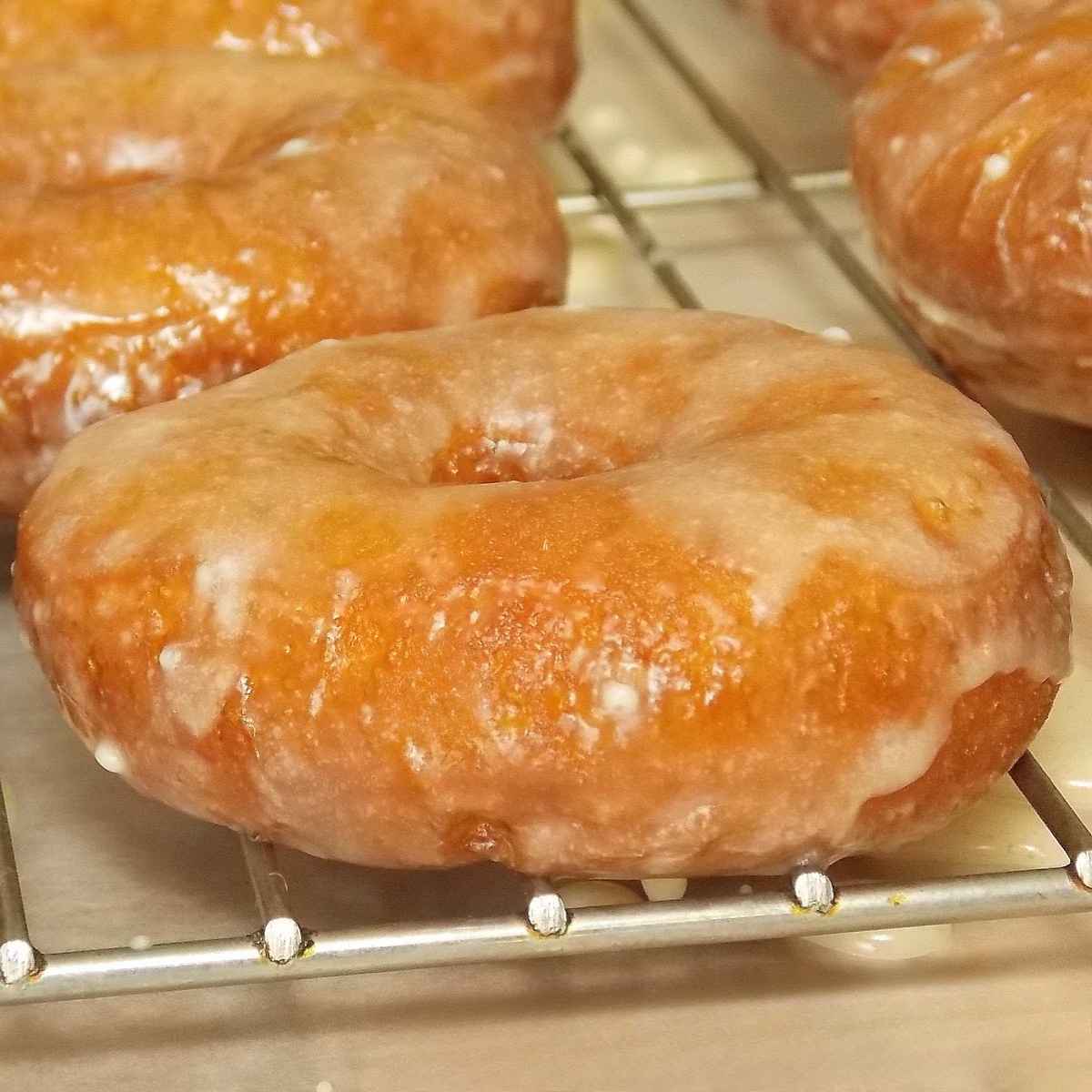 Close up of a soft cider glazed doughnut with a shiny cider glaze, highlighting the ender yeast donut crumb.