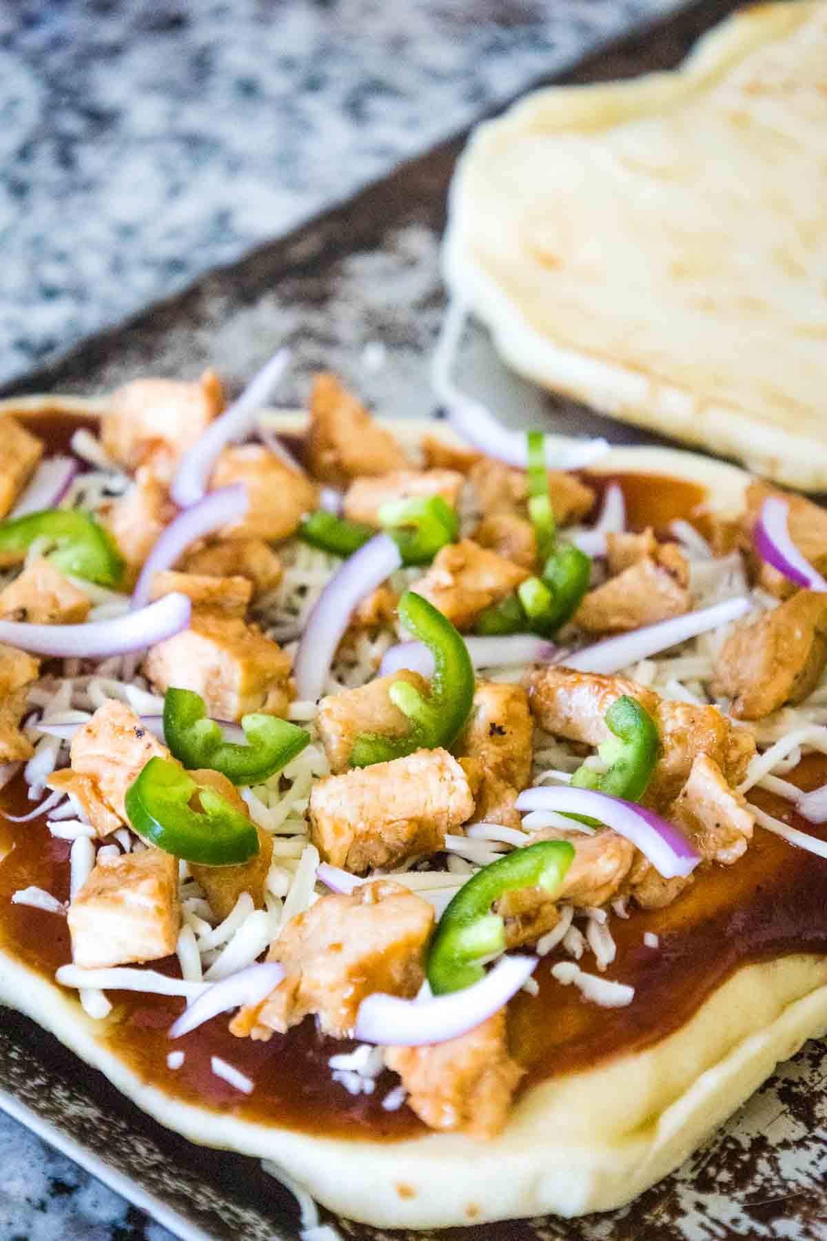 Unbaked BBQ Chicken Naan Pizza topped with barbecue sauce, chicken, jalapenos, red onion, and mozzarella.