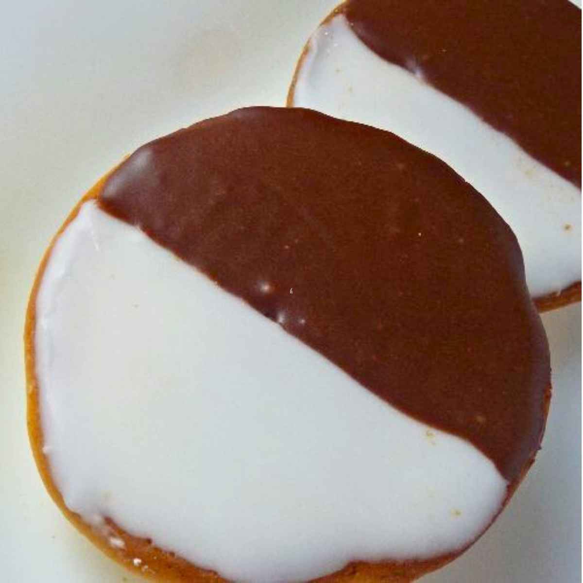 Upclose image of two cookies frosted with ½ chocolate icing and ½ white icing on a white plate.