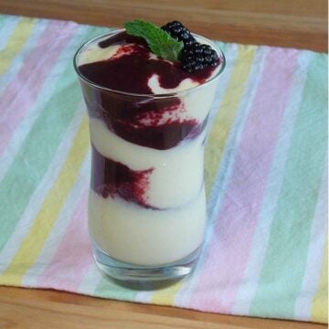 A clear glass with layers of blackberry and mango smoothie mixture, topped with fresh blackberries and a mint leaf.