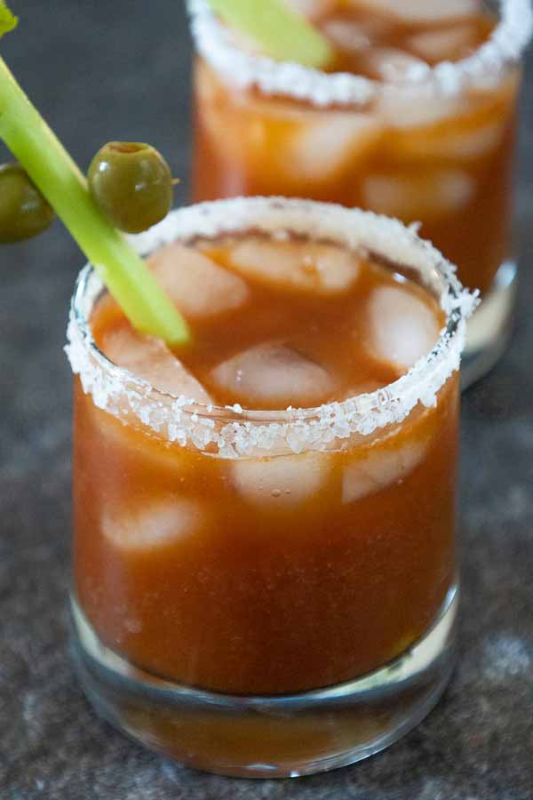 Two glasses of Chipotle Blood Mary cocktails with salted rims, garnished with celery stalks and green olives.