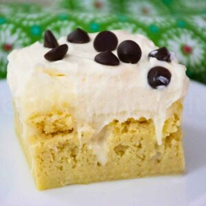Close up of a slice of keto cannoli poke cake with creamy ricotta frosting and chocolate chips.