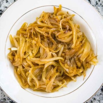 Golden brown caramelized onions piled on a white plate with a thin gold rim.