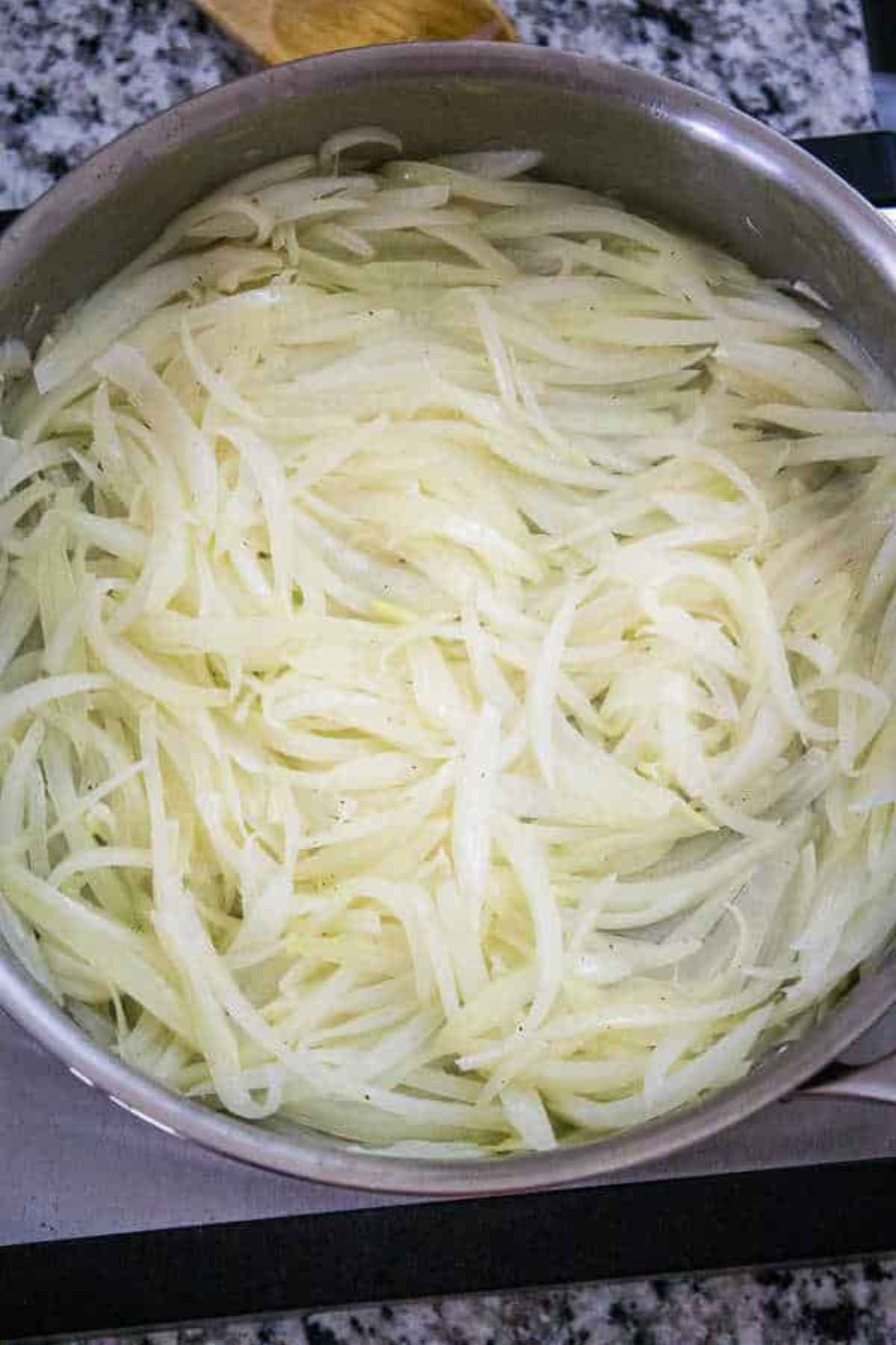 Freshly sliced raw onions spread in a stainless steel pan before cooking.