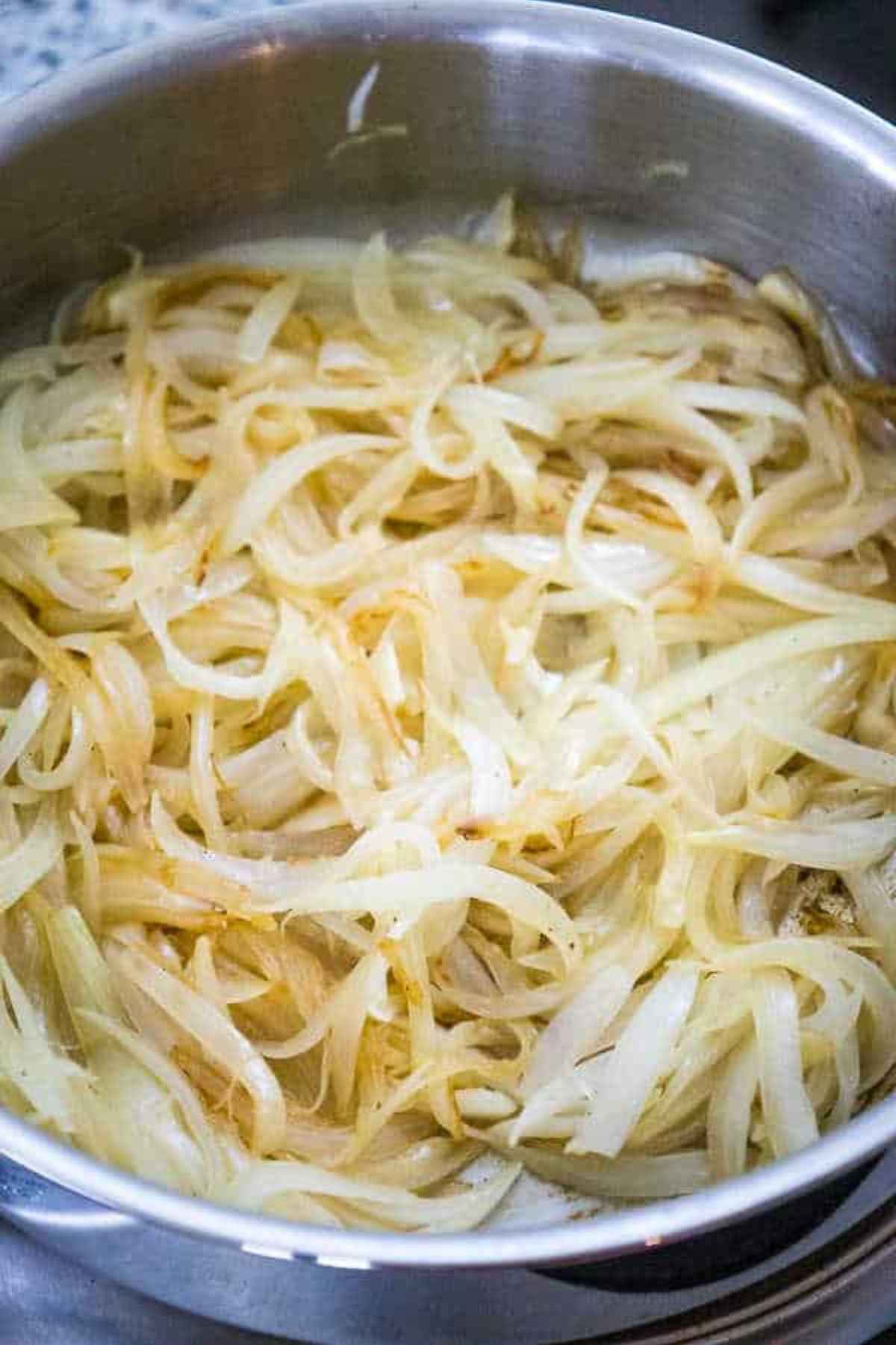 Lightly golden onions cooking in a stainless steel pan, starting to caramelize.